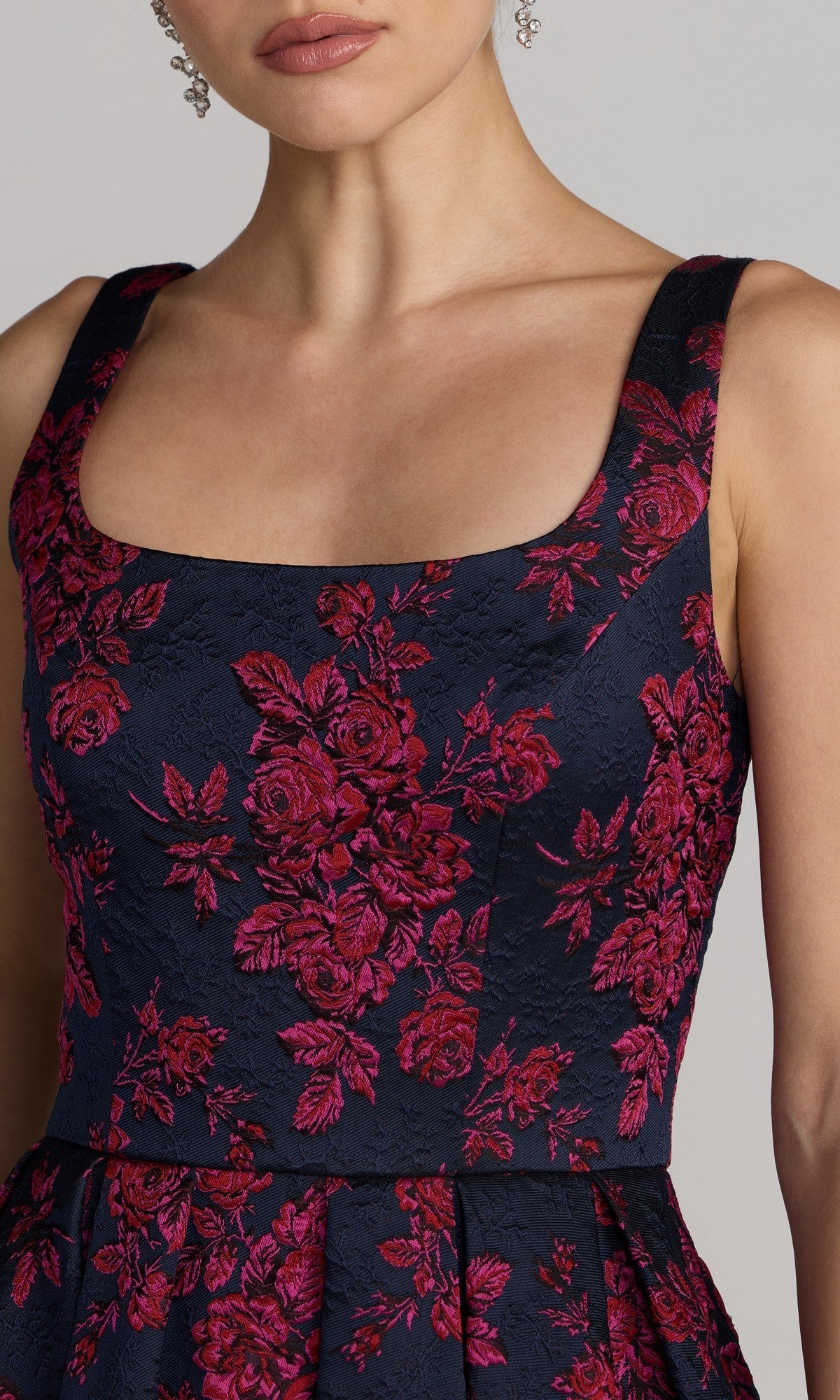 Woman wearing the Mac Duggal 68625 tea-length party dress in navy, featuring a sleeveless design with a square neckline and red floral embroidery, shown from shoulders to waist.